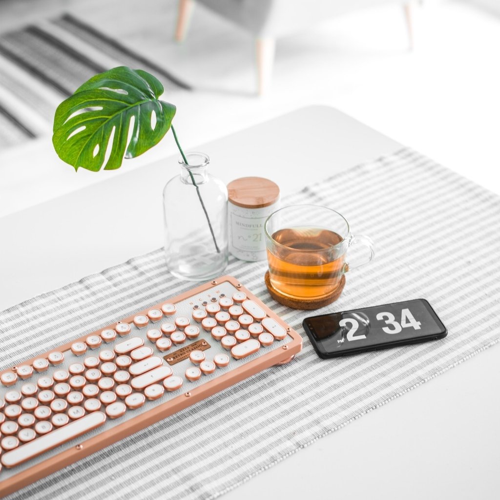 desk with leaf in vase, a drink, a keyboard and a clock with white background